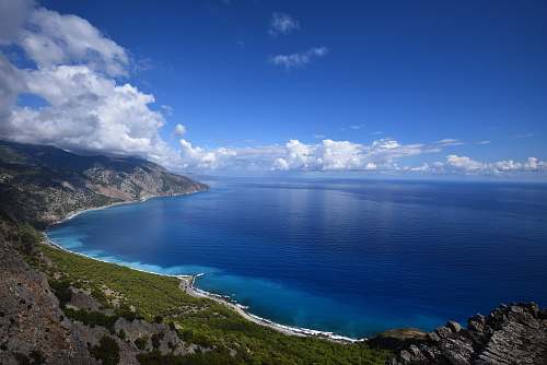 water blue ocean water beside mountain under blue and white cloudy sky ocean