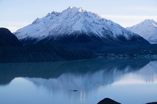 outdoors calm lake in between snow covered mountain during daytime mountain