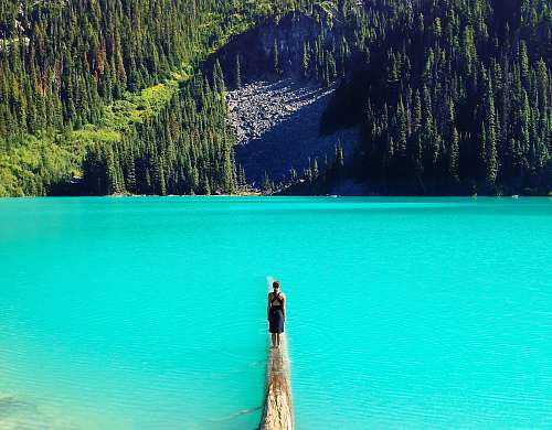 water landscape photography of man standing on dock lake