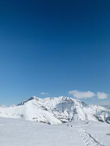 outdoors people standing on snowy field and mountain under blue and white sky during daytime mountain