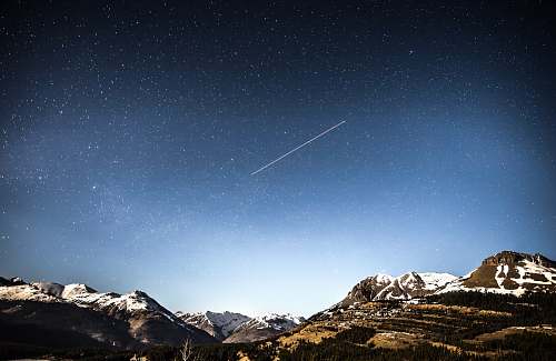 mountain photo of shooting star over snow covered mountains sky