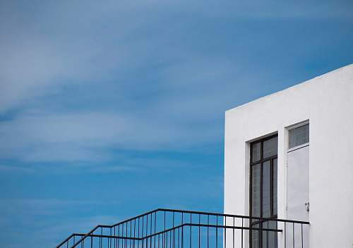 banister white building with black staircase under blue sky handrail
