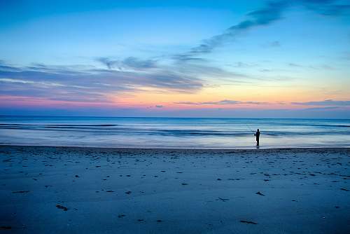 ocean silhouette of person fishing on shallow part of sea beach