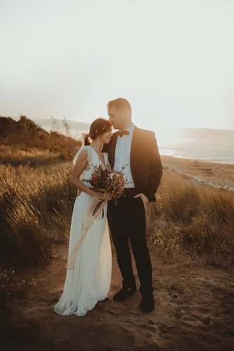 clothing man in black formal suit beside white sleeveless dress person