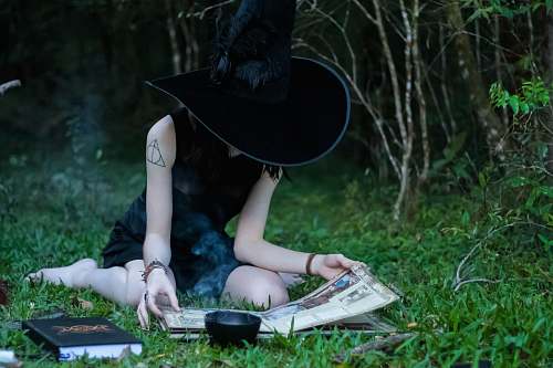 clothing woman reading book while sitting on green lawn grasses hat