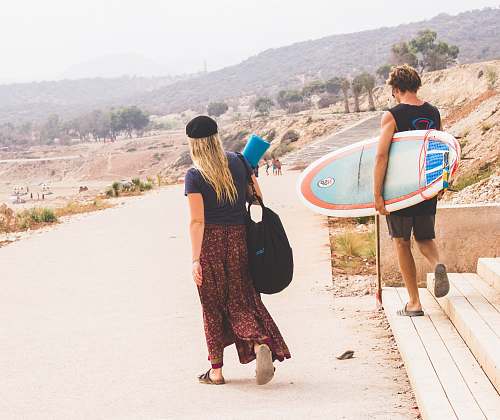 person man holding surfboard while walking with woman people