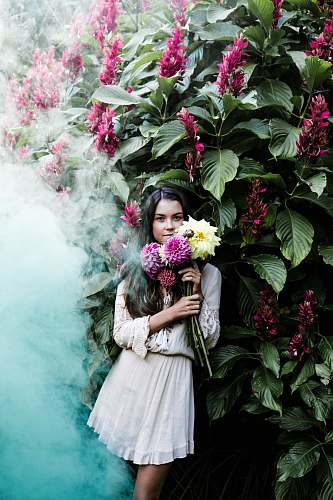 person woman holding yellow and purple flowers leaning back on green leafed plants with flowers people