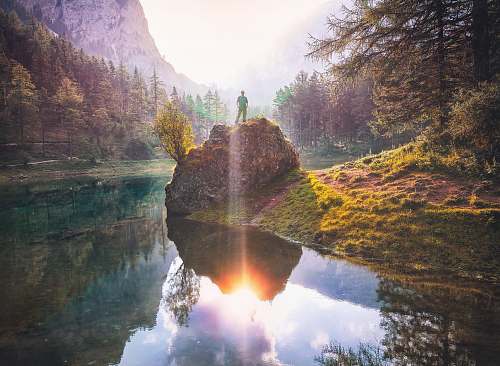 flare man standing on rock beside lake person