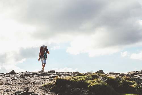 person man in white shorts walking on rocky road under white sky during daytime human