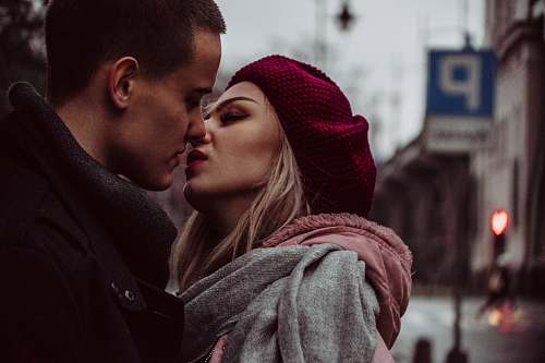 human man and woman standing while kissing beside street signage people