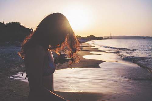 human silhouette photo of woman standing on seashore during golden hour people