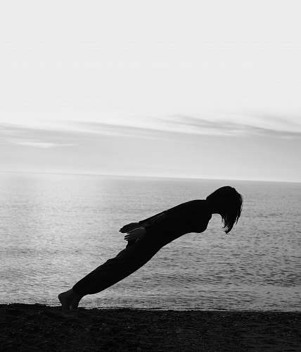 grey person doing gravity lean on the shore black-and-white
