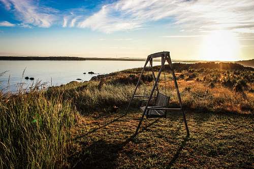 outdoors gray wooden bench swing facing body of water surrounded by grass swing
