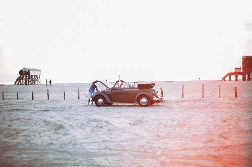 car woman looking to vehicle engine near peoples at daytime sand