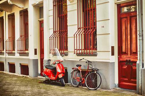 door red motor scooter parked beside house bicycle