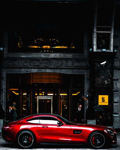 automobile red coupe parked in front of black and gray building during daytime transportation
