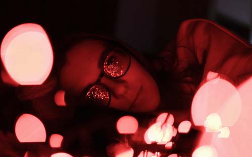 person bokeh photography of woman wearing eyeglasses while lying people