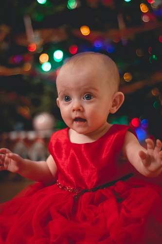 person child in red satin dress by Christmas tree baby
