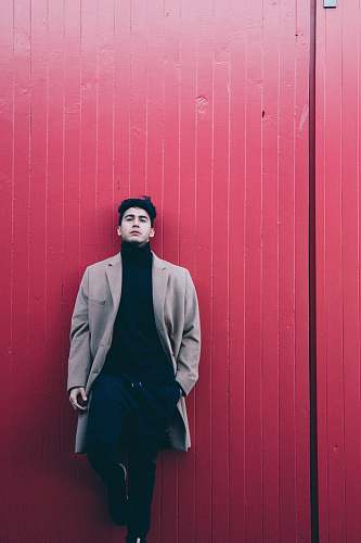 person man wearing coat leaning on red wall people