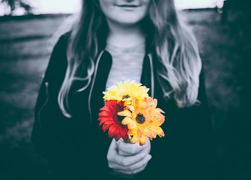 person selective-color photo of person holding yellow and red flowers woman