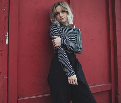 person woman in gray top leaning her back on red wall people
