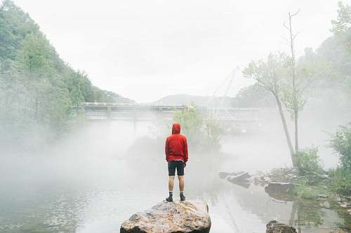 standing man standing on rock facing foggy creek lake