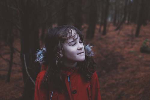person girl wearing red coat standing near trees girl