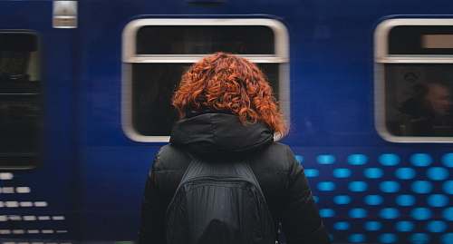 human woman wearing black hooded jacket and black backpack standing in front of moving blue train person
