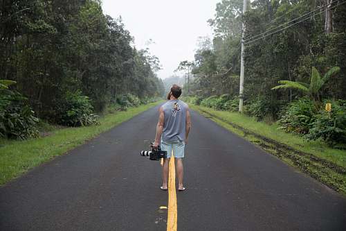 human man standing in the middle of the street carrying black and gray video camera road
