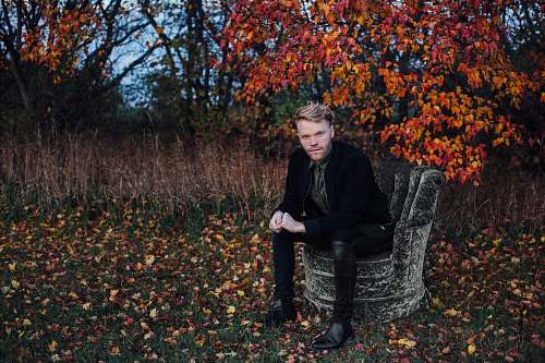 people man wearing black suit sits on black concrete chair beside brown tree human