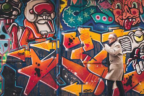 graffiti man wearing grey coat walking beside wall with graffiti human