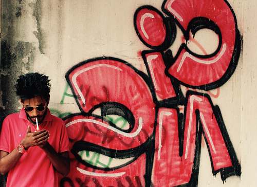 graffiti photo of man holding lighter lighted cigarette beside wall human