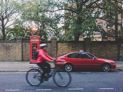 human time lapse photography of person riding bike near red sedan and telephone booth car