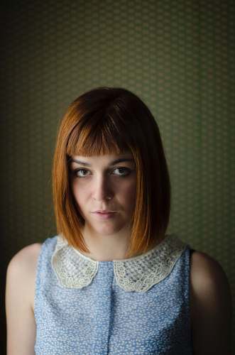 people woman in blue floral sleeveless top in front of a wall portrait