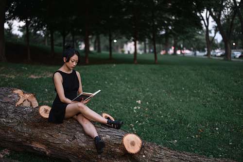 people woman reading book while sitting on fallen tree trunk human