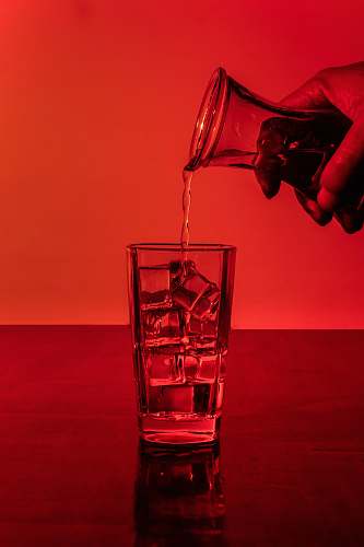 glass person pouring water in glass with ice cubes alcohol