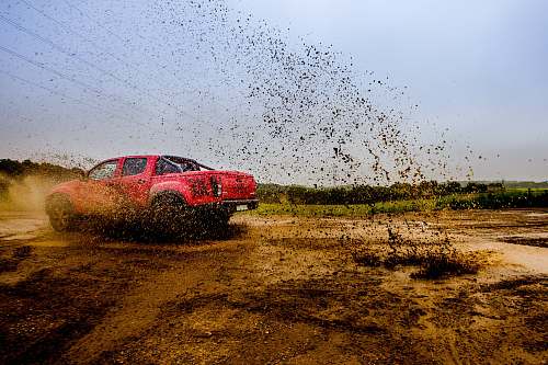 belgium red 4-door truck on mud near trees under cloudy sky dirt road