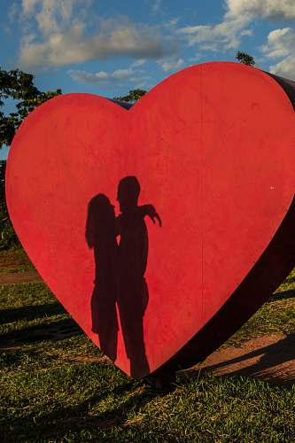 human shadow of coupe hugging near red heart statue person