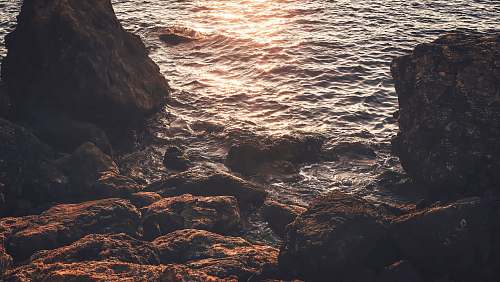 sea rock near seat reflect light on water at daytime ocean