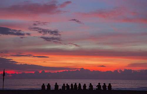 people people sitting on seashore while watching golden hour sunrise