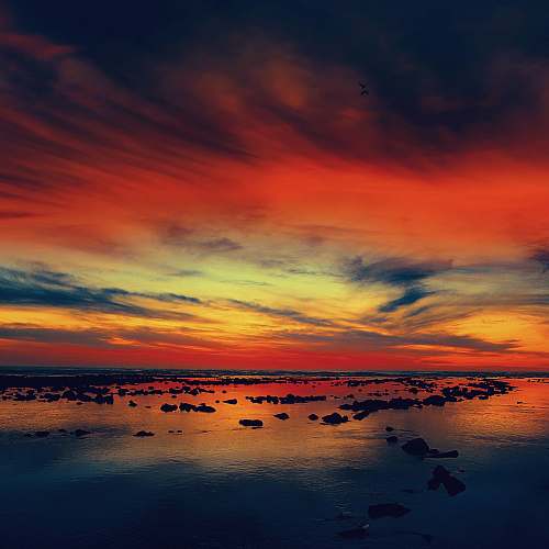 sunset silhouette of rocks on body of water under red and blue clouds dusk
