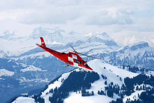 snow photo of flight of red and white rescue helicopter during snow daytime glacier