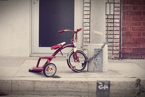 bicycle red and white Radio Flyer trike chained on stone post bike