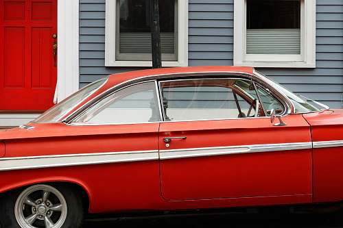 car classic red coupe parks beside gray and white wooden house automobile