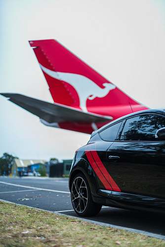 transportation red and white airplane behind a black hatchback automobile