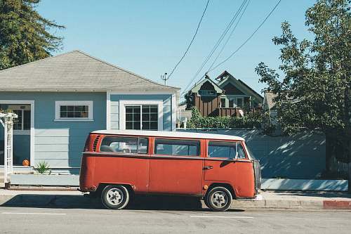 van red Volkswagen Samba parked in front of teal house caravan