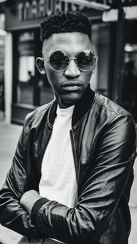people grayscale photo of man wearing bomber jacket standing outdoor during daytime person