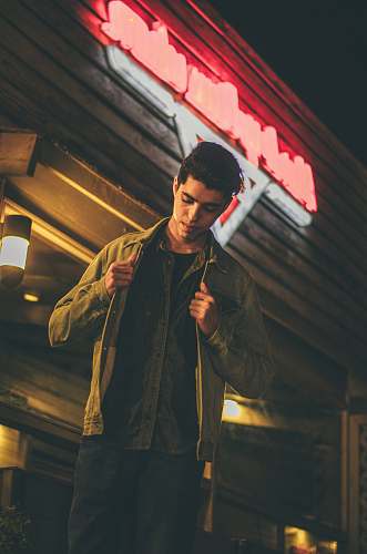 people man holding his brown jacket and standing in front of brown concrete storefront low-angle photo person