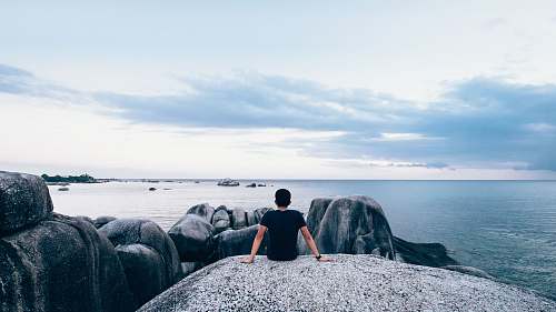 people man sitting on rock beside body of water sea