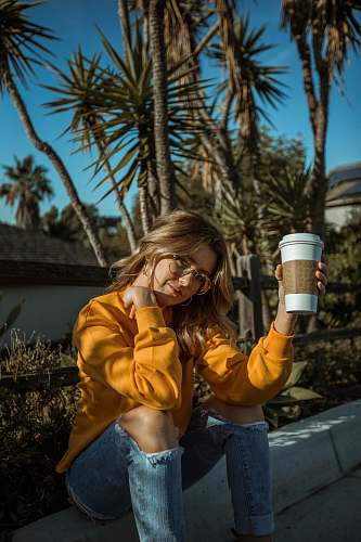 people woman sitting on curb while holding disposable cup at daytime person